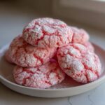 A stack of bright pink, crinkle-top strawberry cake mix cookies dusted heavily with powdered sugar.