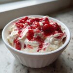 Close-up of a white bowl filled with creamy strawberry cheesecake dip topped with bright red strawberry preserves.