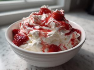 A white bowl filled with fluffy strawberry cheesecake dip, topped generously with whipped cream and strawberry sauce.