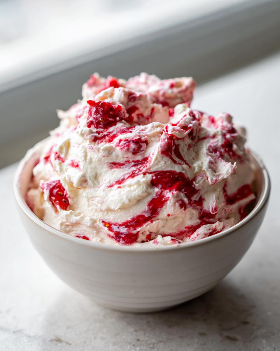 A close-up of fluffy strawberry cheesecake dip swirled with bright red strawberry sauce in a white bowl.