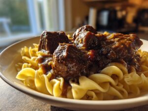 Close-up of tender crockpot beef tips covered in rich brown gravy served over wide egg noodles.