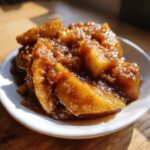Close-up of thick, caramelized apple pie filling coated in cinnamon sugar, served in a small white bowl.