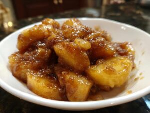Close-up of thick, glossy apple pie filling chunks coated in cinnamon sugar sauce in a white bowl.