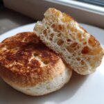 A toasted english muffin sliced in half, showing the characteristic open crumb structure and golden-brown nooks on the surface.