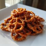 A pile of shiny, amber-colored toffee pretzels coated in a sweet glaze, resting on a white square plate.