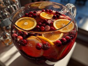 Close-up of a glass bowl filled with bright red Thanksgiving punch, garnished generously with floating orange slices and whole cranberries.