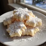 A stack of light, star-shaped whipped shortbread cookies heavily dusted with powdered sugar on a white plate.