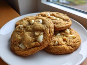 A stack of three golden brown white chocolate macadamia nut cookies with visible white chocolate chunks on a white plate.