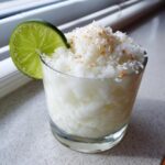 A frozen white Christmas margarita topped with toasted coconut flakes and a fresh lime wheel.