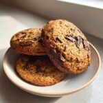 Close-up of three thick, moist banana bread cookies loaded with dark chocolate chunks on a small plate.