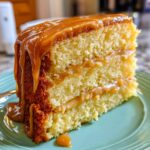 Close-up of a moist slice of caramel cake recipe layered with filling and topped with dripping caramel sauce.