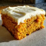 A close-up, sunlit square of moist carrot cake bars topped with thick cream cheese frosting.