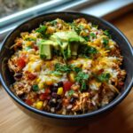 A close-up of a hearty chicken burrito bowl topped with melted cheese, fresh avocado slices, and cilantro.