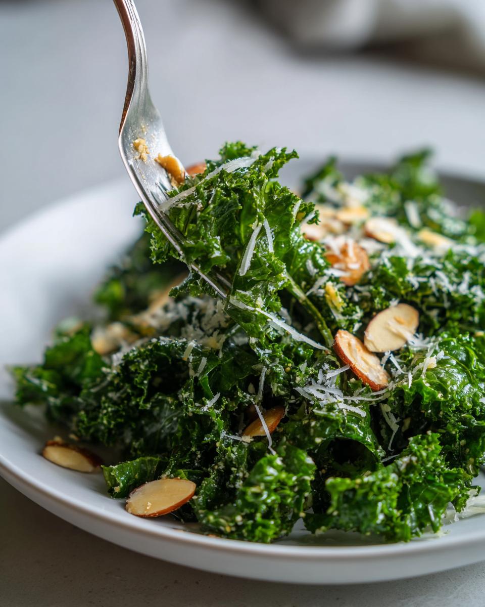 A fork lifts a bite of vibrant green kale salad topped with shaved Parmesan cheese and sliced almonds.