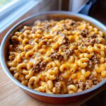 A skillet filled with steaming hot cheesy taco pasta featuring elbow macaroni, seasoned ground beef, and melted cheddar cheese.