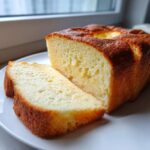 Close-up of a golden-brown cottage cheese bread loaf with one slice cut and resting beside it on a white plate.