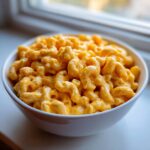 A close-up of creamy, bright orange cottage cheese mac and cheese served in a white bowl near a window.