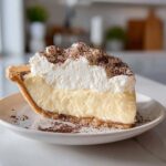 A perfect slice of creamy eggnog pie featuring a thick custard layer and tall whipped topping dusted with cocoa.