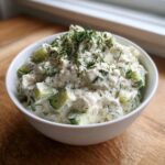 A white bowl filled with creamy pickle dip chunks and topped with fresh dill garnish.