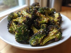A white bowl filled with perfectly crispy roasted broccoli florets sprinkled with Parmesan cheese.