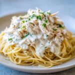 Close-up of crock pot angel chicken shredded meat in creamy sauce over spaghetti pasta, garnished with parsley.