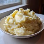 A large bowl filled with fluffy, creamy mashed potatoes recipe, sitting near a bright window.