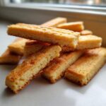 A close-up stack of golden brown, rectangular shortbread cookies with fork marks visible on top.