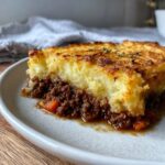 A close-up of a serving of cottage pie showing rich meat filling and a browned, crispy mashed potato topping.