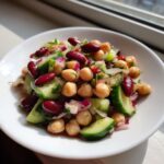 A vibrant bowl of high protein bean salad featuring chickpeas, kidney beans, cucumber chunks, and red onion.
