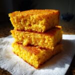 Three square pieces of golden yellow hot water cornbread stacked on a white napkin.