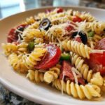 Close-up of a serving of italian pasta salad featuring rotini pasta, salami, tomatoes, olives, and grated cheese.