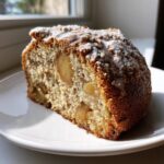 Close-up of a moist slice of Jewish apple cake with visible apple chunks and a light sugar glaze.