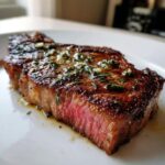 Close-up of a juicy, perfectly seared ribeye steak cooked medium-rare, topped with herbs and garlic butter.