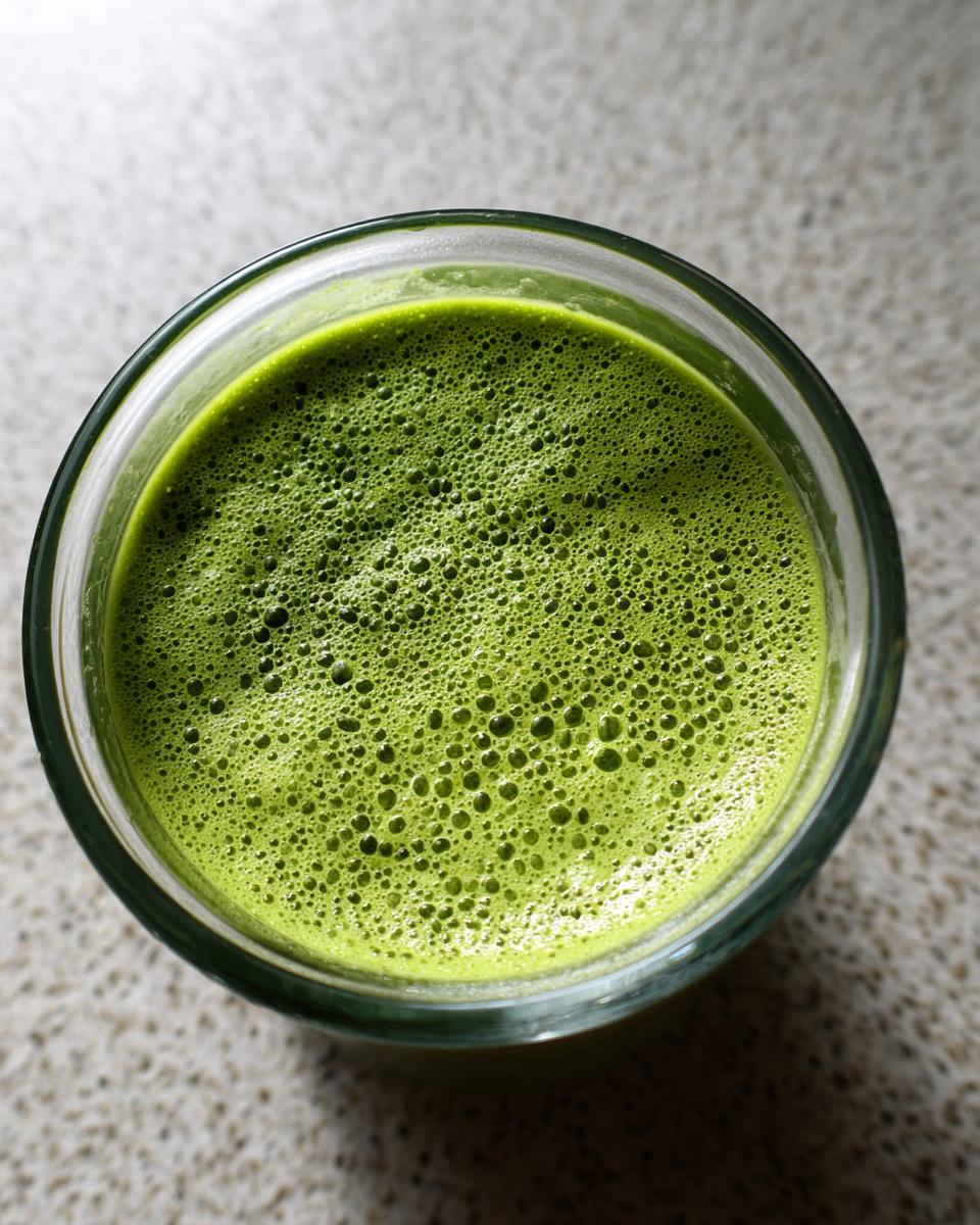 Overhead view of bright green matcha chia pudding mixture with small foam bubbles in a clear glass.
