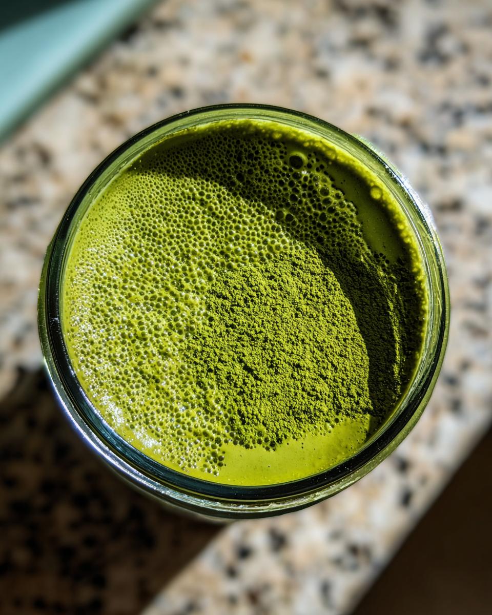 Overhead view of bright green matcha chia pudding in a glass, topped with dry matcha powder.