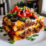A thick, layered slice of mexican pizza topped with melted cheese, black olives, tomatoes, and green onions.