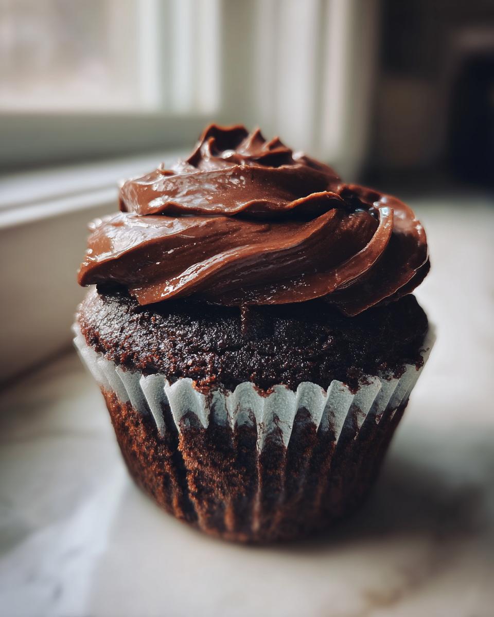 Close-up of a single, moist chocolate cupcake topped with thick, swirled chocolate frosting.