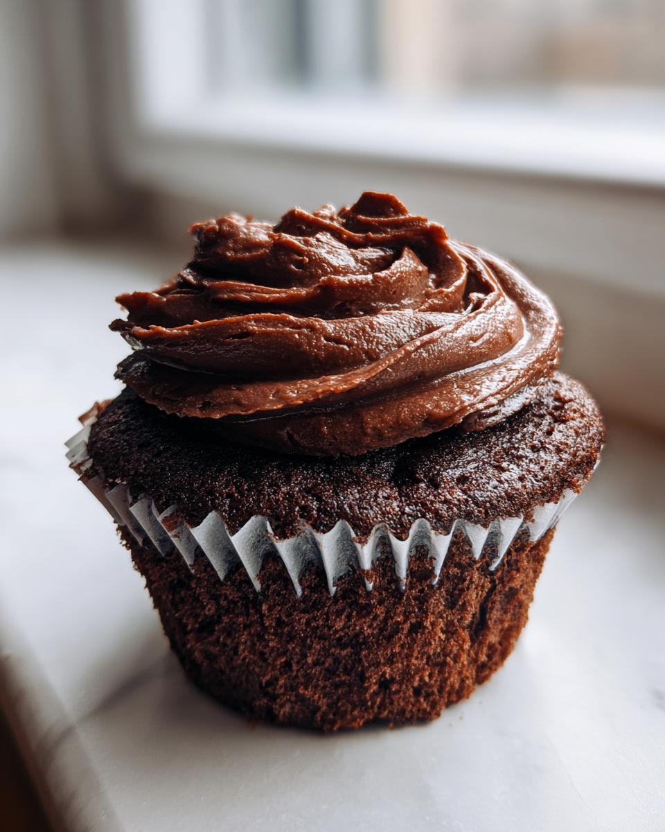 Close-up of a single, moist chocolate cupcake topped with a swirl of rich chocolate frosting.