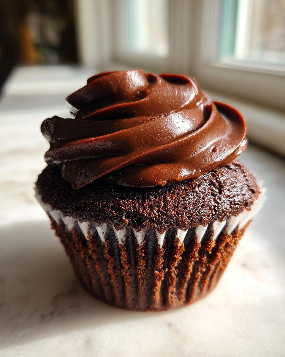 Close-up of a single, moist chocolate cupcake topped with a swirl of dark chocolate frosting.