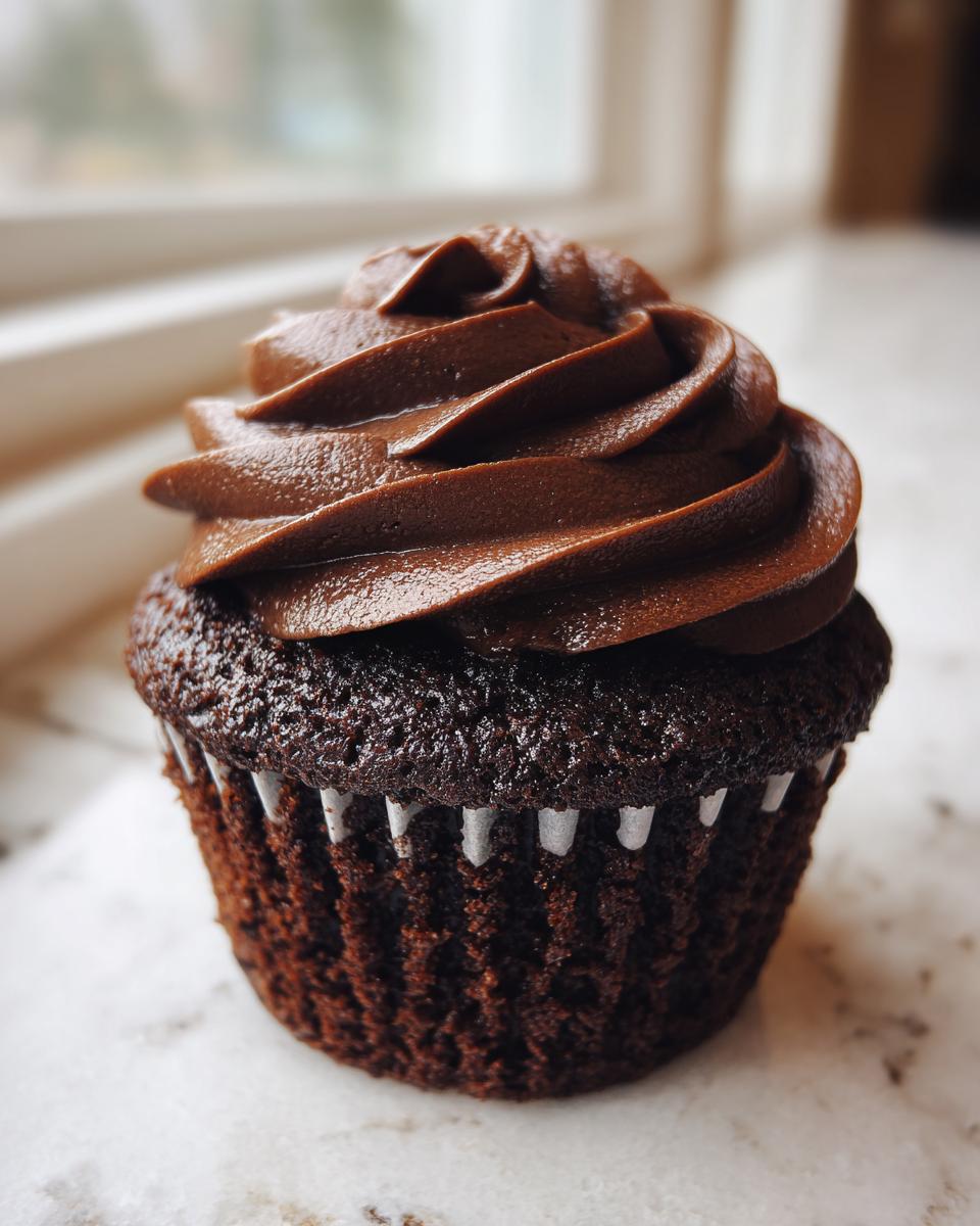 Close-up of a single, moist chocolate cupcake topped with a swirl of dark chocolate frosting.
