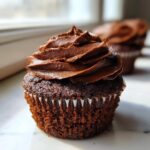 Close-up of a moist chocolate cupcake topped with a generous swirl of rich chocolate frosting.