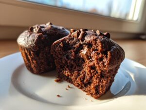 Close-up of two moist chocolate muffins, one cut in half showing the rich crumb and chocolate chips.