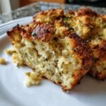 Close-up of a portion of moist homemade stuffing with a golden-brown, crispy top sprinkled with herbs.