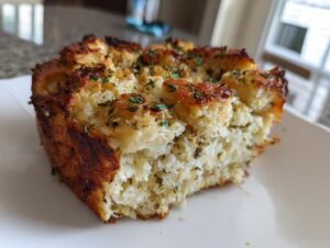 A close-up of a serving of moist homemade stuffing with a crispy, browned top sprinkled with herbs.