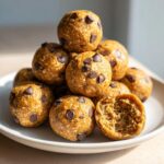 A stack of homemade peanut butter protein balls studded with chocolate chips on a white plate.