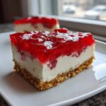 Close-up of a square slice of pretzel salad featuring a crumbly crust, creamy filling, and bright red strawberry gelatin topping.