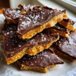 Close-up of broken pieces of homemade toffee recipe topped with dark chocolate and flaky sea salt.
