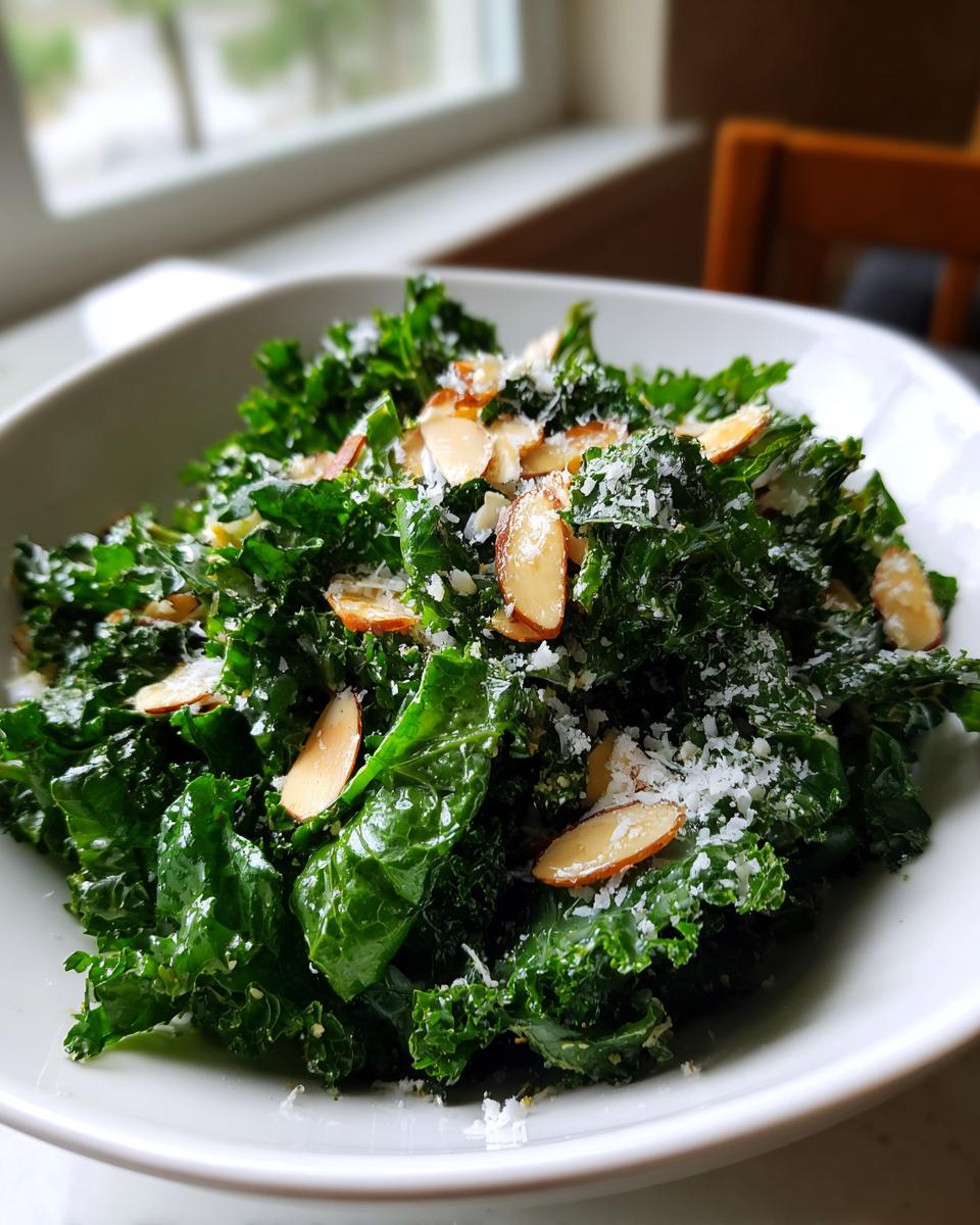 Close-up of a fresh kale salad topped with toasted sliced almonds and grated Parmesan cheese.