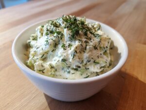 Close-up of a creamy, chunky pickle dip topped generously with fresh chopped dill.