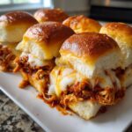 Close-up of gooey melted cheese oozing over shredded chicken filling in baked bbq chicken sliders on soft rolls.